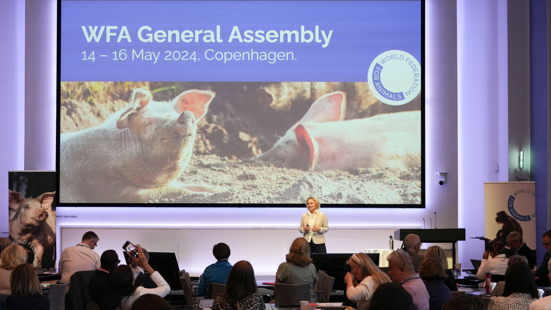 Direktør Britta Riis står på scenen og taler til WFA General Assembly kvinde står på scene og taler foran mennesker