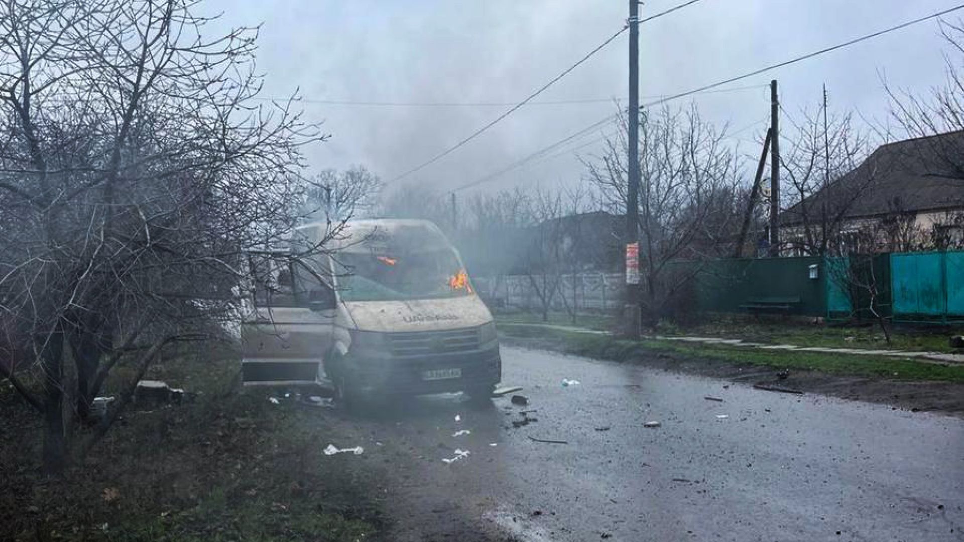 En varevogn er blevet ramt af en russisk drone i Ukraine, den holder på våd vej i gråt vejr. Luften er fuld af røg, og der er stadig flammer i bilens forrude.