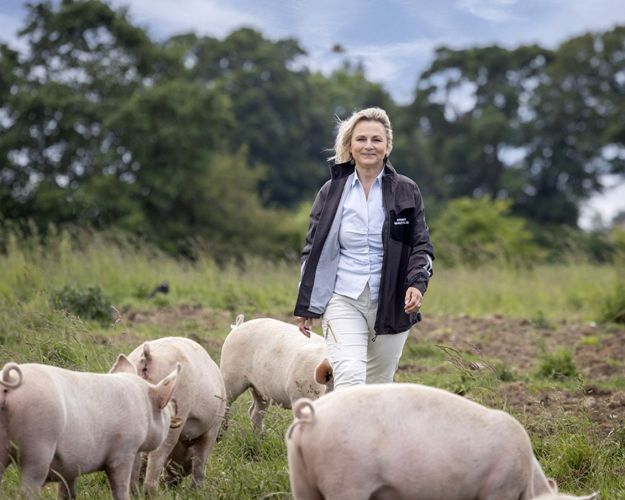 Britta Riis på en mark med grise og træer i baggrunden