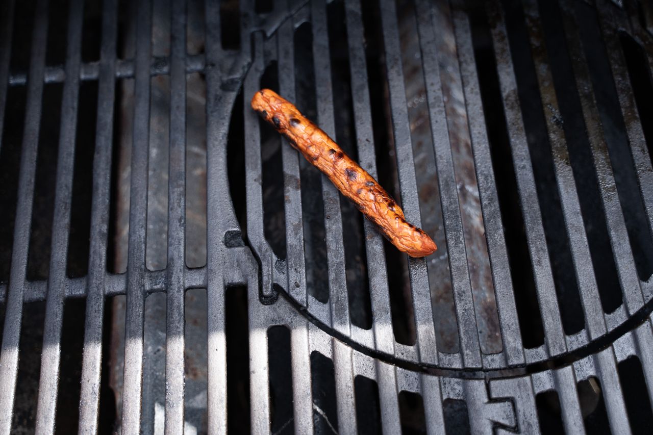 Plantebaseret pølse ligger på grill med sprækket skind. 
