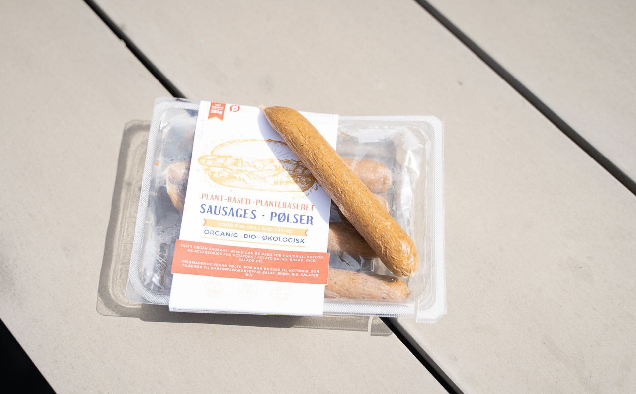 Pølse ligger ovenpå pølsepakke på et bord udenfor. 