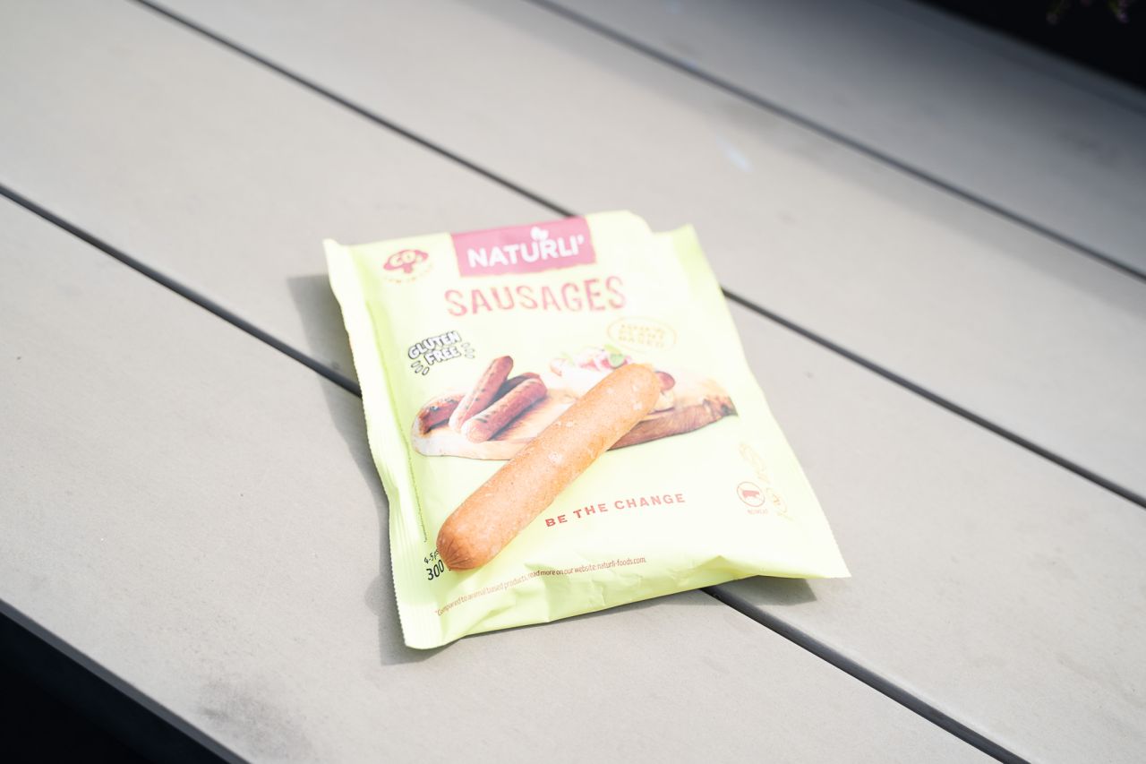 Gullig pose med veganske grillpølser, hvor én af pølserne er taget ud og lagt ovenpå. 