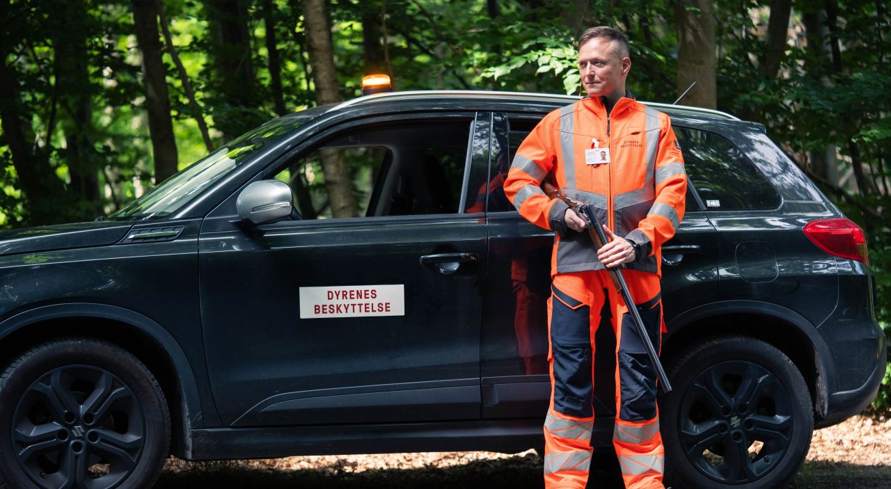 skytte i orange tøj står foran en sort bil med skriften dyrenes beskyttelse på
