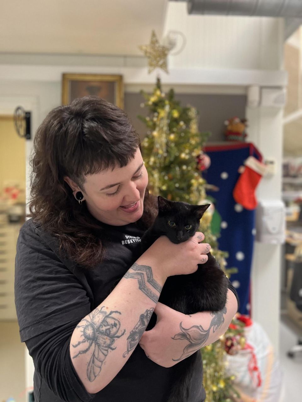 Nana med kat - Kvinde holder en sort kat i armene foran et pyntet juletræ.