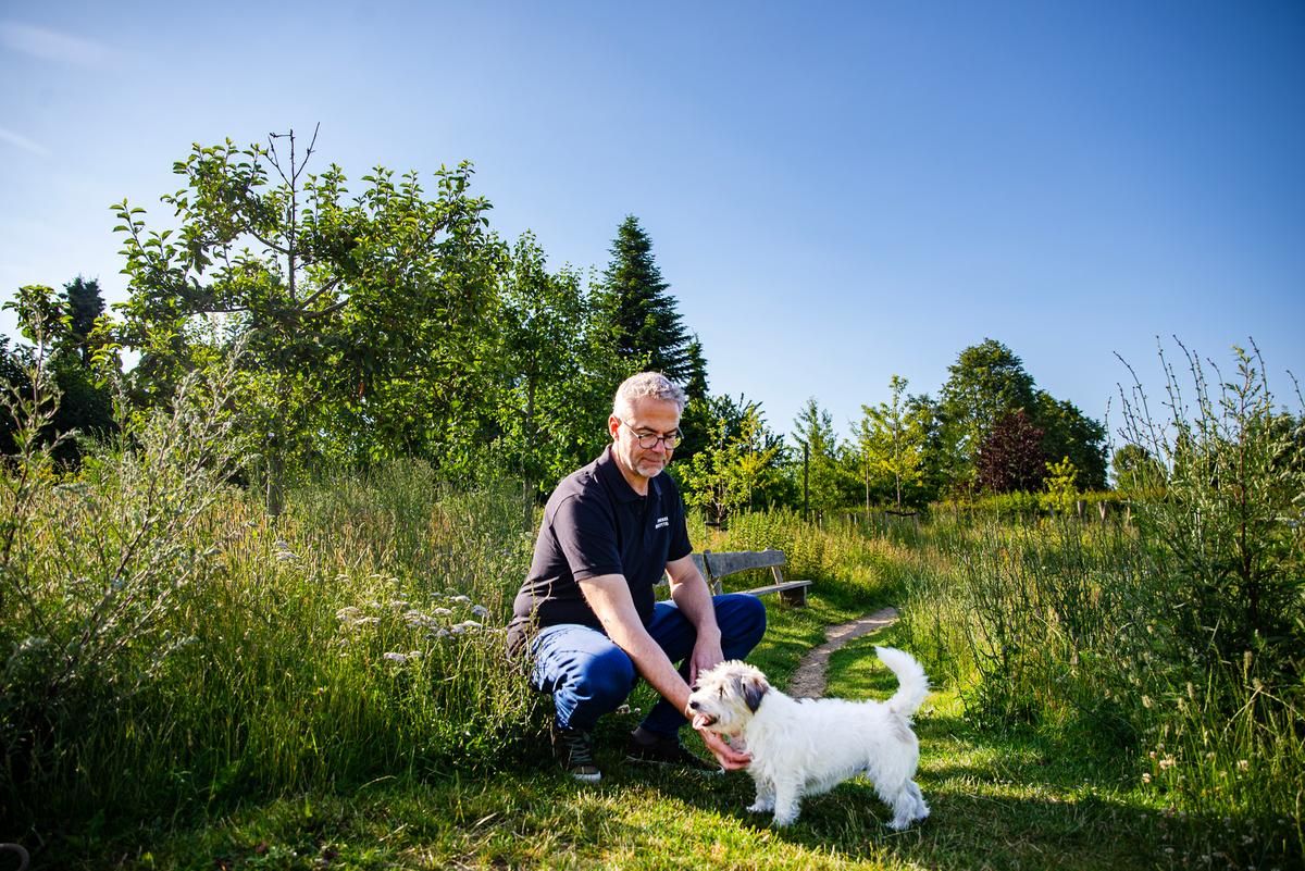 Jens Jokumsen sidder i det grønne og kæler med en lille hvid hund.